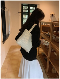 Close-up of white quilted tote bag with heart embroidery in a cozy cafe setting