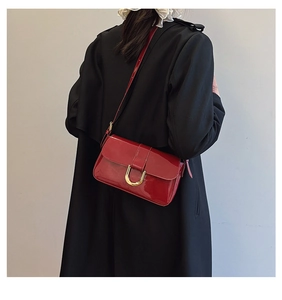 Model wearing a wine red glossy leather shoulder bag with gold horseshoe buckle detail
