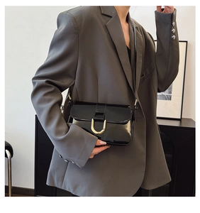Detail of black patent leather shoulder bag with gold metal horse-bit buckle on a model