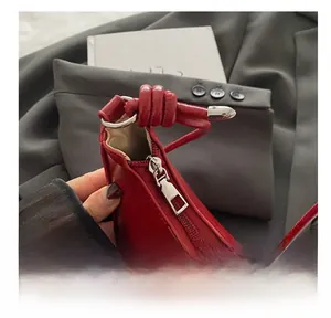 Detail of red leather crescent bag featuring smooth zipper and knotted strap with metal accents