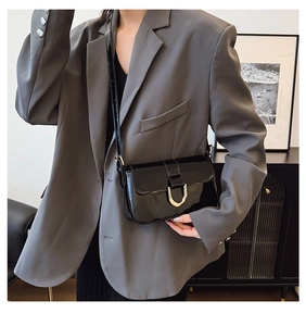 Detail of a black patent leather shoulder bag with gold horseshoe buckle on a model