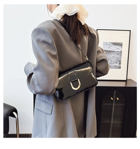 Detail of black patent leather underarm bag with gold metal buckle on grey blazer