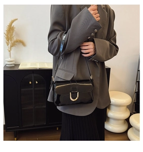 Close-up of black patent leather crossbody bag with elegant gold metal hardware