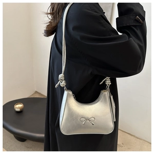 Silver metallic moon-shaped shoulder bag with bow detail and braided strap on model