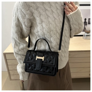 Detailsicht der schwarzen Stepptasche mit goldenem H-Verschluss auf weißem Pullover