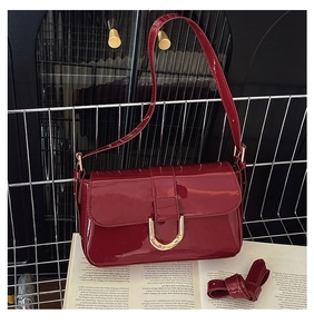 Detail of burgundy patent leather shoulder bag with gold horse-bit buckle on vintage books