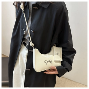 Detail of white patent leather shoulder bag with silver bow and knot strap design