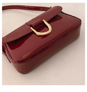 Detailed macro view of dark red glossy patent leather handbag with gold horseshoe buckle