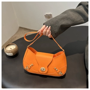 Detailed shot of orange leather underarm bag with gold twist lock and metal rivet studs