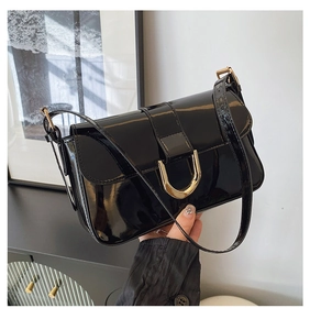 Detail of glossy black leather shoulder bag with elegant golden horseshoe metal buckle