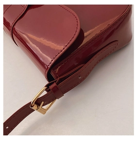 Close-up of deep red patent leather shoulder bag with gold buckle and fine stitching