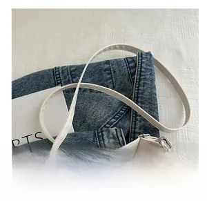 Close-up of white synthetic leather shoulder strap with durable metal buckle on denim