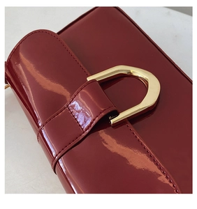 Macro shot of glossy burgundy patent leather bag with a golden U-shaped buckle detail