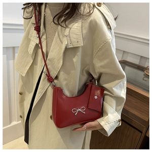 Detail of red leather shoulder bag with silver bow charm and knotted strap on a model