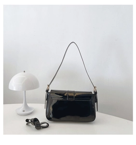 Detail view of black patent leather shoulder bag with glossy finish and gold hardware