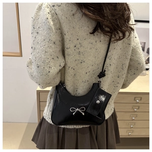 Detail of black patent leather bow bag with mini pouch charm worn by a model