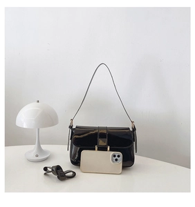 Glossy black patent leather shoulder bag shown next to a smartphone for size reference