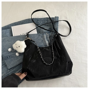Detail of black pleated shoulder bag with silver chain strap and white cloud charm accessory