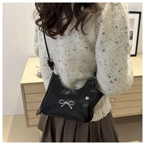 Detail of black patent leather bag featuring a silver metal bow and detachable coin purse
