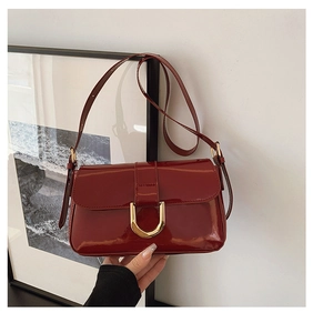 Detail of burgundy patent leather handbag featuring a glossy finish and gold horseshoe buckle