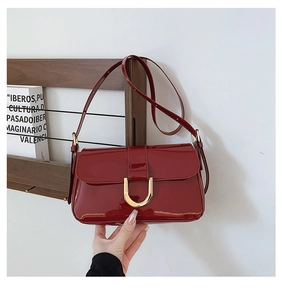 Detail of red patent leather shoulder bag with a shiny finish and gold horseshoe buckle