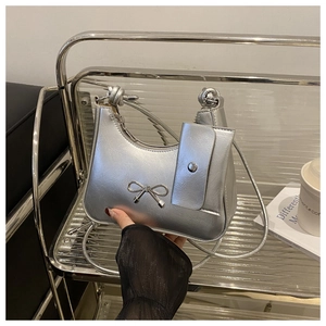 Silver metallic hobo bag with bow detail and matching mini pouch held by model