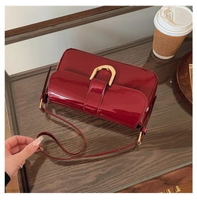Detail of burgundy patent leather handbag featuring a gold D-shaped buckle and fine texture