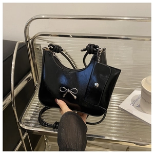 Detail of glossy black handbag featuring silver bow and mini coin purse attachment