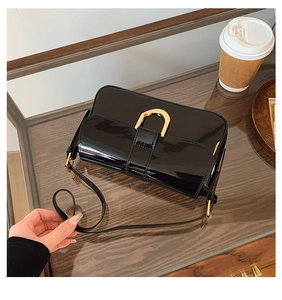Detail of black patent leather crossbody bag with golden horseshoe buckle and mirror finish