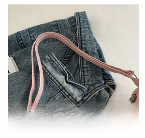 Detail of pink nylon shoulder bag with slim straps and silver zipper on denim background