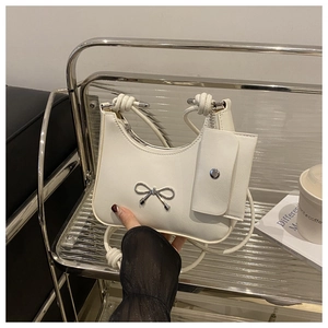 Detail of creamy white crescent shoulder bag with metallic bow and coin purse attachment