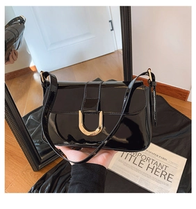 Close-up of a black patent leather shoulder bag featuring a shiny gold horseshoe buckle