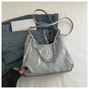 Detail of silver pleated hobo bag with metal chain handle and adjustable strap on soft fabric