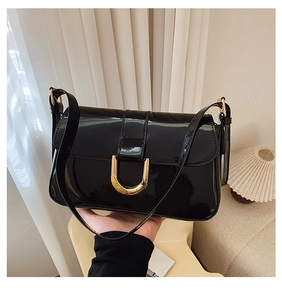 Detail of glossy black patent leather shoulder bag featuring a gold horseshoe buckle