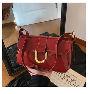 Detail of burgundy patent leather shoulder bag featuring a gold horseshoe buckle
