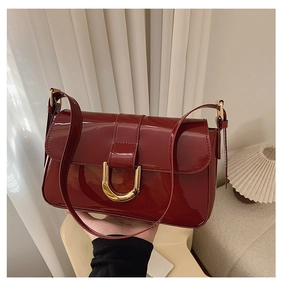 Detail of dark red patent leather shoulder bag with gold horseshoe buckle and strap