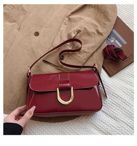 Detail of red glossy patent leather shoulder bag featuring gold U-shaped metal buckle