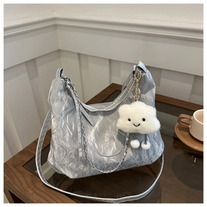 Detail of silver metallic pleated hobo bag with cute cloud charm on wooden table