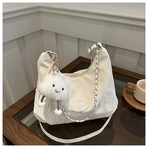 Detail of off-white pleated shoulder bag with silver chain and plush cloud charm on a table