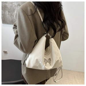 Detail of ivory hobo bag with silver butterfly emblem and chain shoulder strap