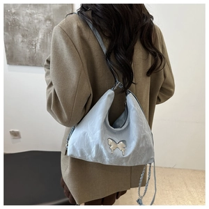 Detail of light blue cloud-textured hobo bag with a silver butterfly and chain strap