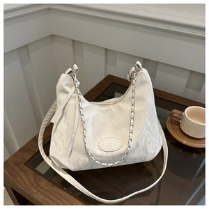 Detail of white pleated crescent bag with silver chain and long strap on a table