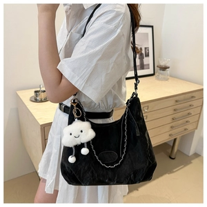 Detail of black glossy pleated hobo bag with silver chain and white cloud plush charm