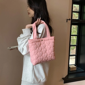 Pink quilted tote bag with heart pattern shown on shoulder in a warm indoor setting