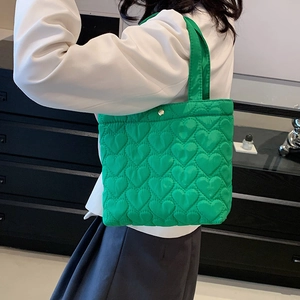 Vibrant green heart-quilted tote bag in nylon fabric worn by a model in a minimal setting