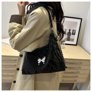Detailed view of black wrinkled glossy shoulder bag with silver metal bow charm on model