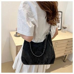 Detail of black pleated shoulder bag with silver chain strap shown in a lifestyle setting