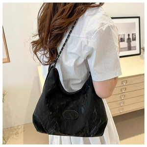 Detail of a black pleated shoulder bag with a chain strap and moon shape design