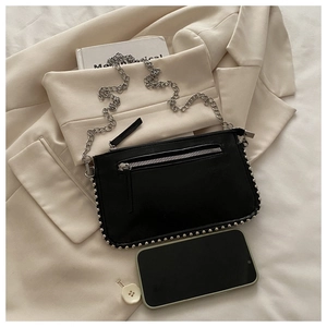 Detail of black crossbody bag with silver rivet trim and metal chain on white blazer background