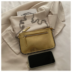 Close-up of golden metallic chain bag with silver rivets next to a smartphone for size